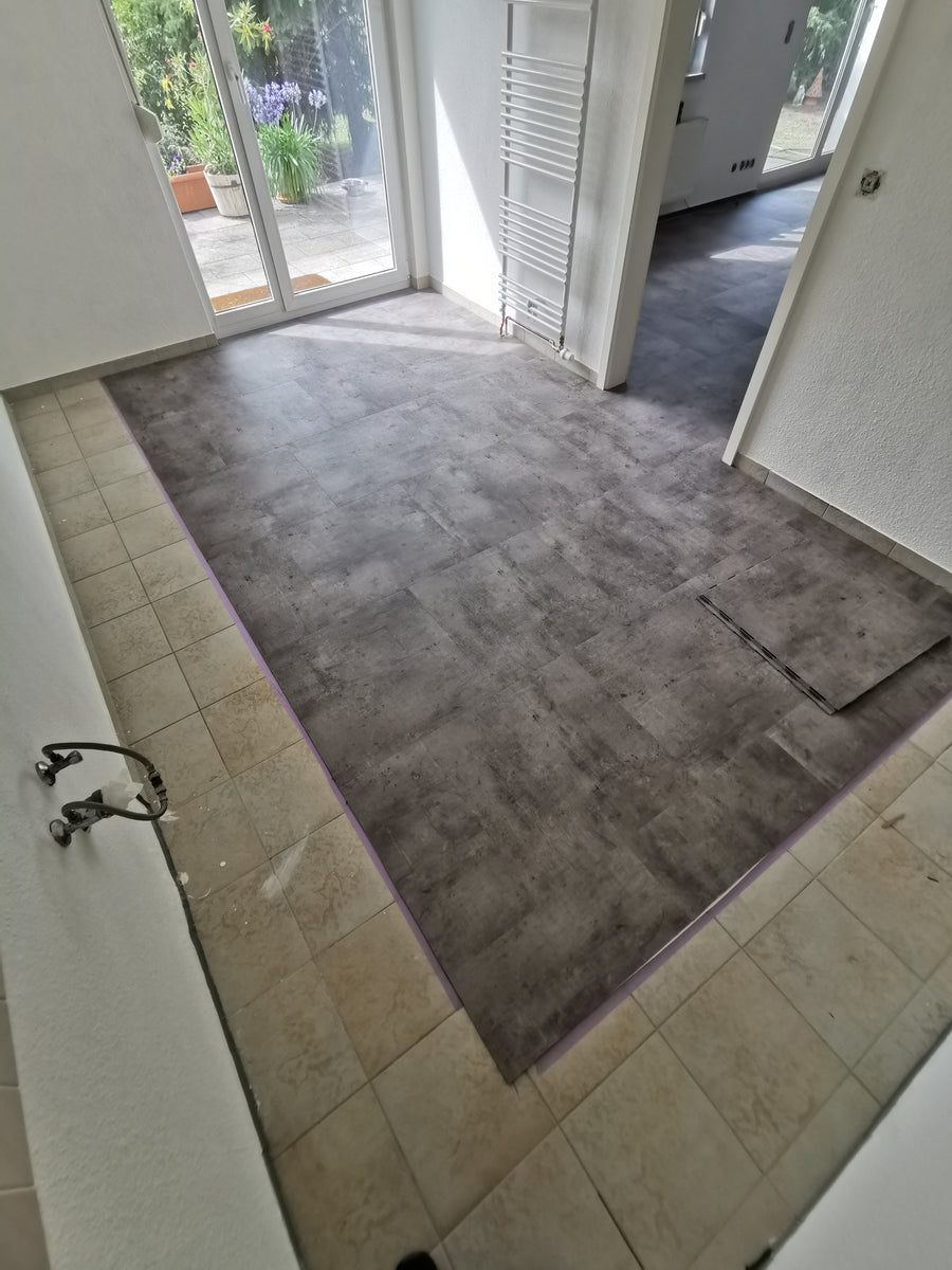 Eingangsbereich mit grauem Klebevinyl in Betonoptik neben altem Fliesenboden