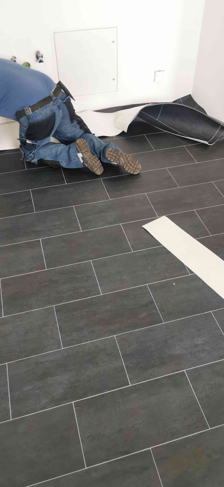 Flur mit anthrazitfarbenem Klebevinyl in Steinoptik, Bodenleger bei der Arbeit